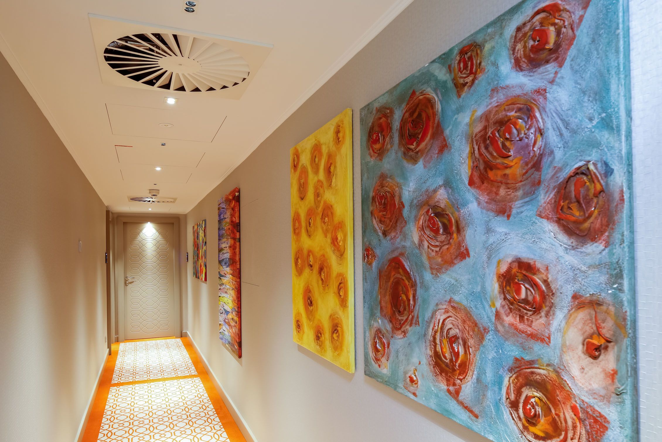 A hallway with a patterned floor, a ceiling fan, and three large floral paintings on the walls.