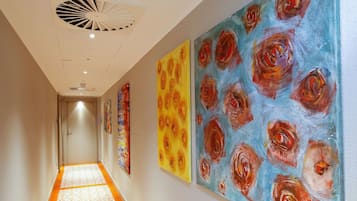 Un couloir doté d’un sol à motifs, d’un ventilateur de plafond et de trois grandes peintures florales accrochées aux murs.