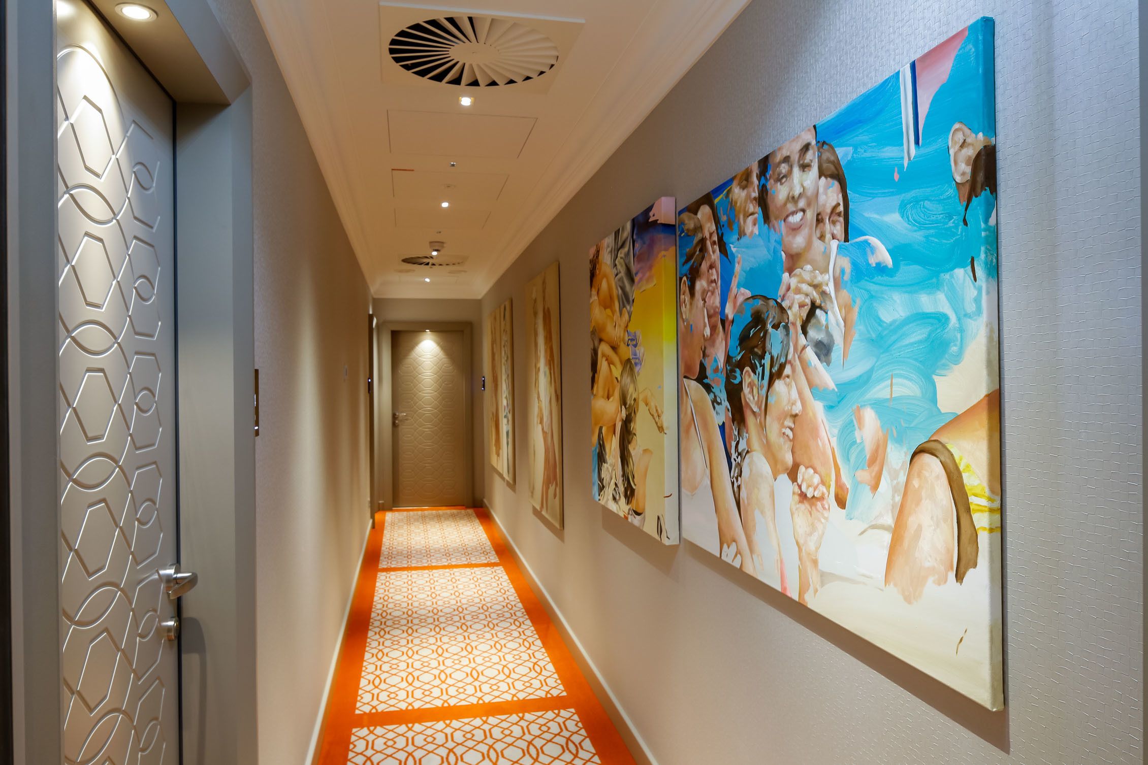 Un pasillo de hotel con piso estampado, obras de arte en las paredes y un ventilador de techo.