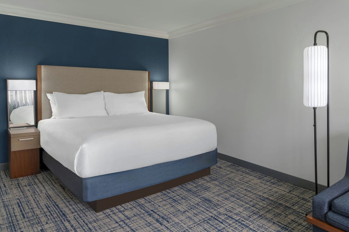A hotel room with a large bed, a nightstand, a lamp, and a floor lamp.