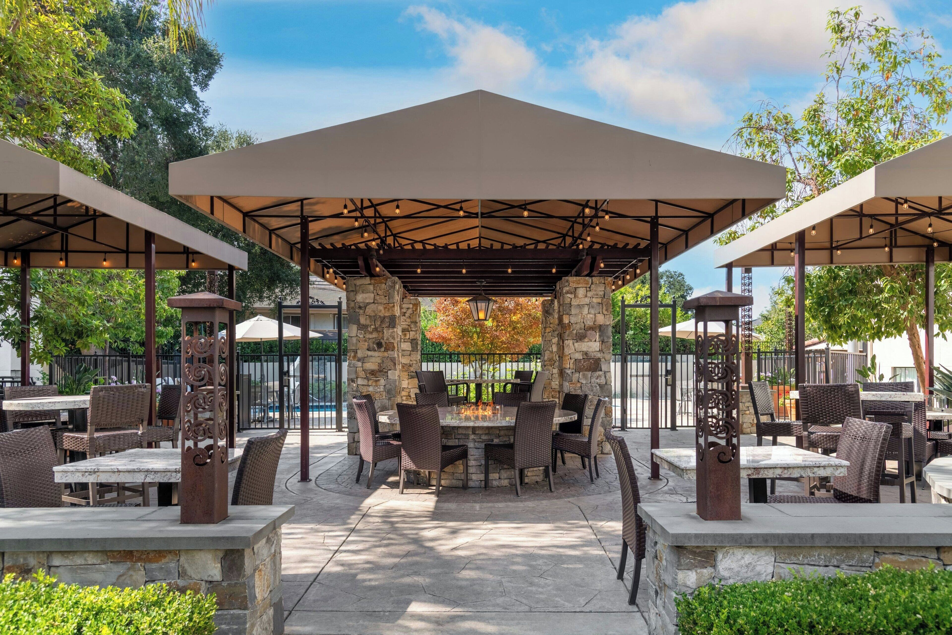 An outdoor patio area with stone pillars, wicker furniture, and a central fire feature.