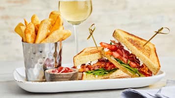 Un plato con un sándwich a la parrilla, una copa de vino blanco y una porción de papas fritas.