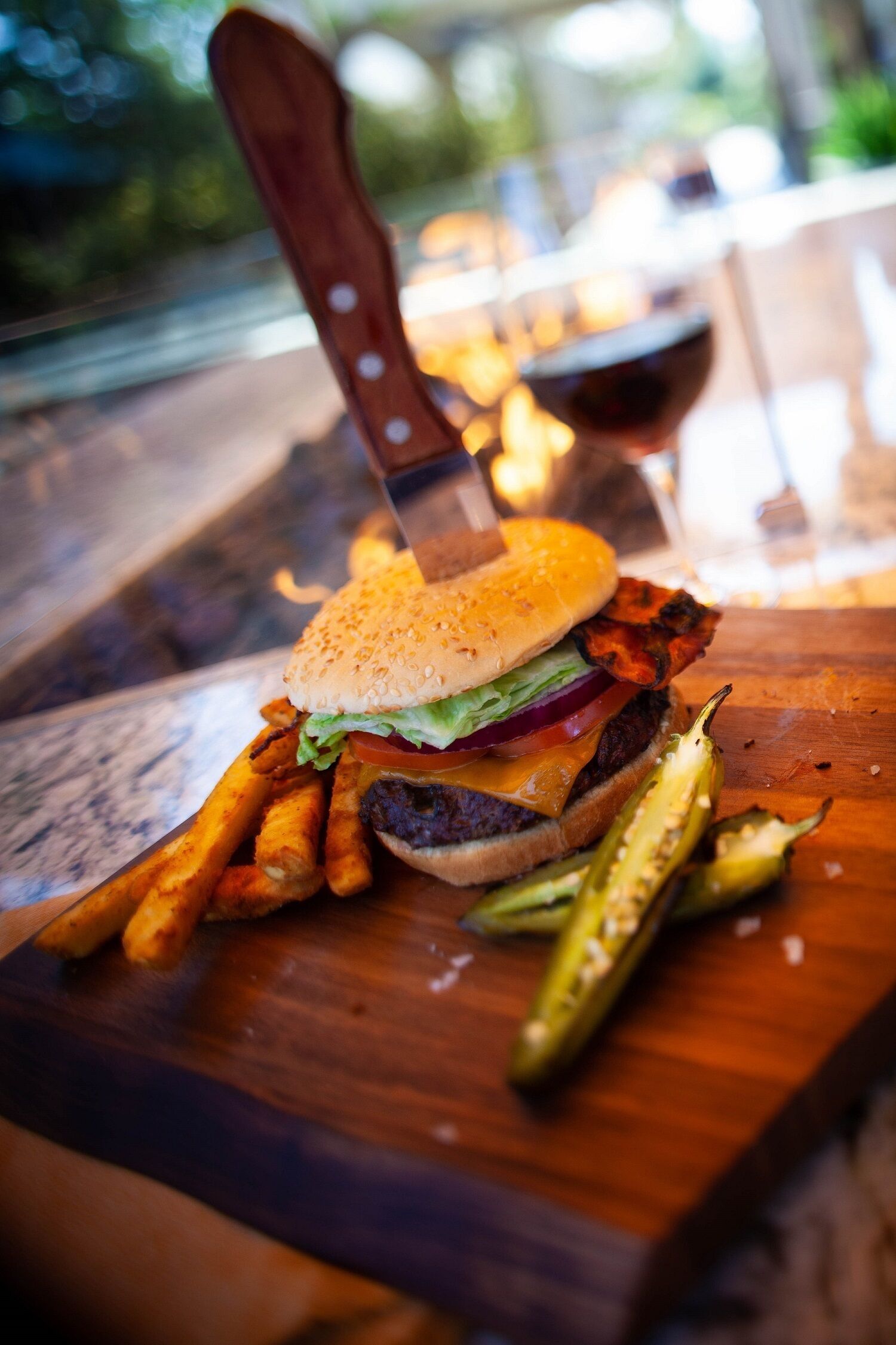 Ein Burger mit Pommes und Essiggurken auf einer Holzplatte.