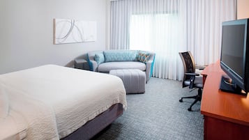 A hotel room with a large bed, a sofa, a desk with a computer, and a TV.