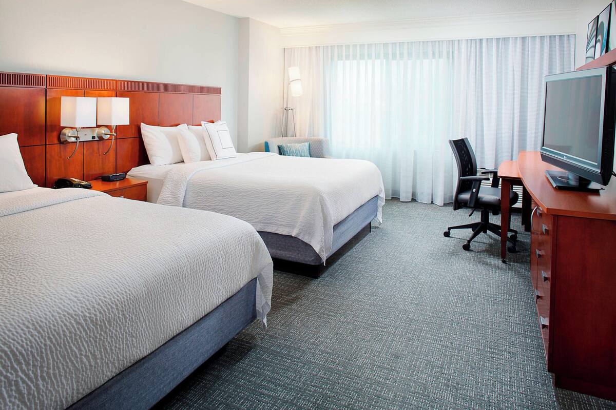 Une chambre d’hôtel avec deux lits, un bureau avec un ordinateur, une chaise et un téléviseur.