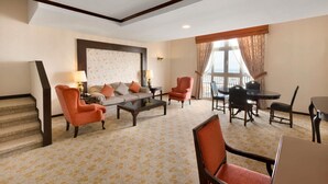 Habitación de hotel con sofá, sillones, mesa de comedor y una escalera.