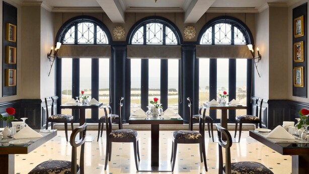 Un comedor con mesas dispuestas para dos, amplias ventanas en arco y vistas al paisaje.