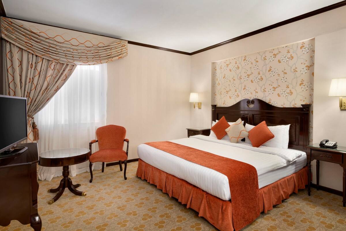 Une chambre d’hôtel avec un grand lit, deux lampes de chevet, une télévision, une petite table et une chaise.