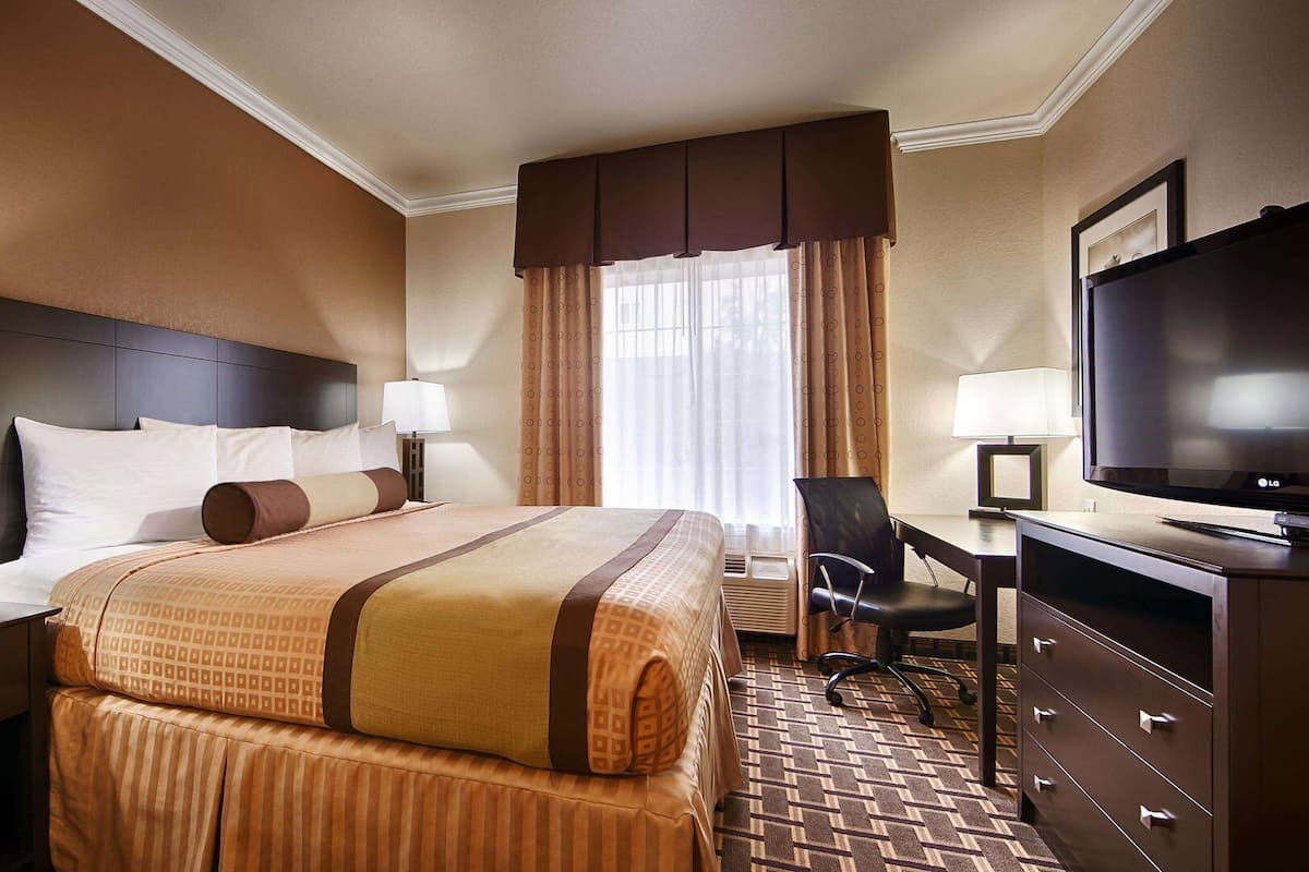 A hotel room with a large bed, a desk with a chair, a television, and a dresser.