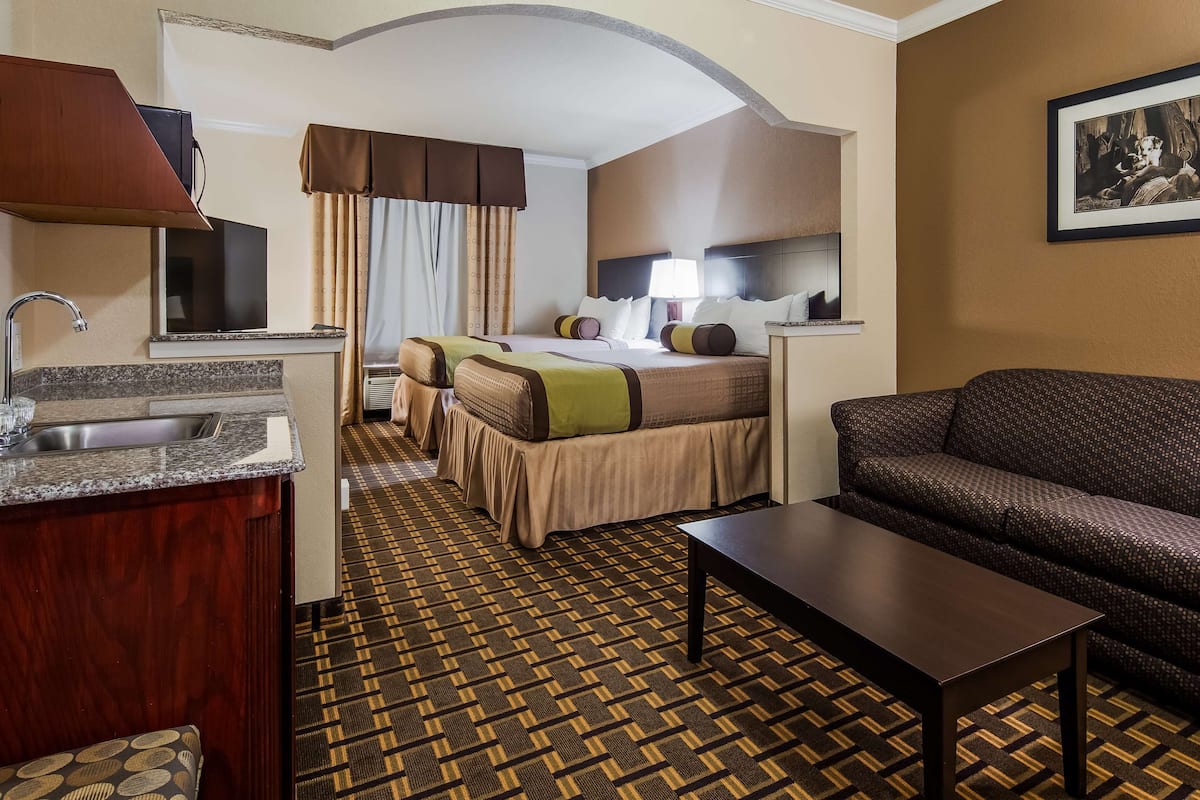A hotel room with a kitchenette, a sofa, a bed with a patterned bedspread, and a framed picture on the wall.