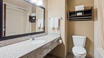 A bathroom with a granite countertop sink, a mirror, a toilet, and a towel rack with folded towels.