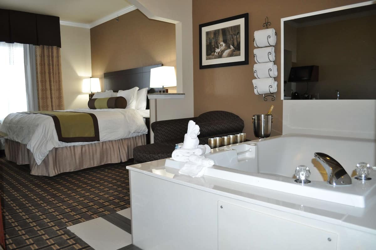 A hotel room with a large bed, a separate sofa, a bathroom with a bathtub, and a flat-screen TV.