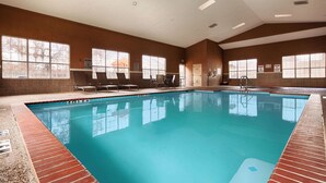 An indoor swimming pool with clear water, surrounded by lounge chairs and tables, large windows, and warning signs. - Best Western Plus Cutting Horse Inn & Suites (Weatherford)