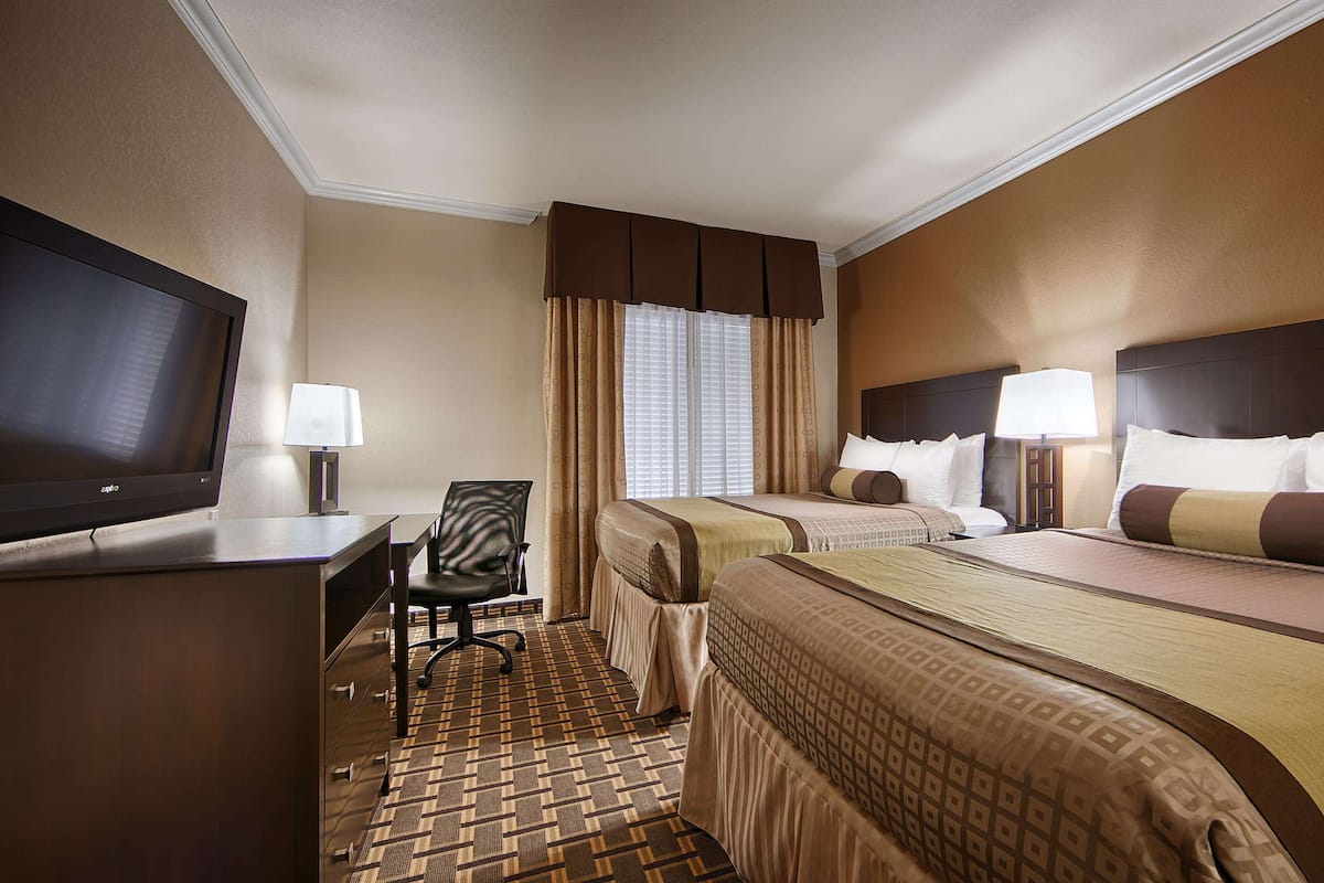 A hotel room with two beds, a desk with a TV, and a chair.