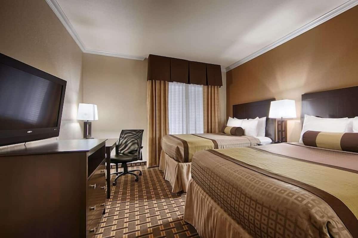 A hotel room with two beds, a desk with a TV, a chair, and a window with curtains.