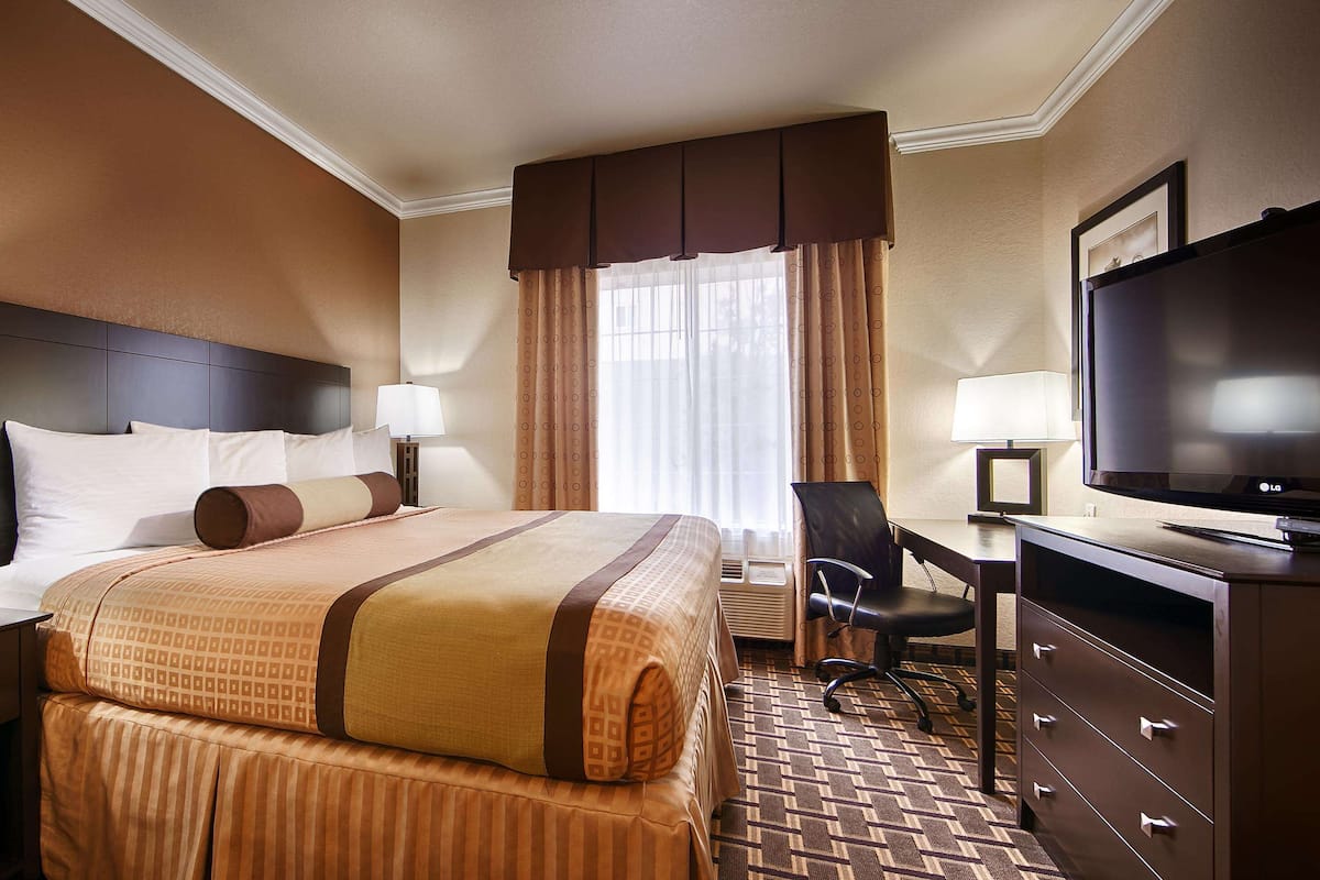 A hotel room with a large bed, a desk with a chair, a television, and a dresser.