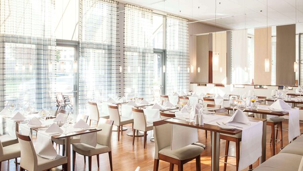 A modern dining area with tables set for service, large windows with curtains, and a clean, contemporary design. - NH Frankfurt Niederrad (Frankfurt)