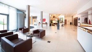 A spacious lobby with a reception desk, seating area, and a staircase leading to upper floors. - NH Frankfurt Niederrad (Frankfurt)