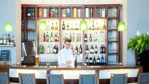 A bar area with a bartender, shelves of liquor bottles, glasses, and bar stools. - NH Frankfurt Niederrad (Frankfurt)