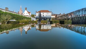 A historic building with a reflection in a calm water body, surrounded by well-maintained hedges and a clear sky. - Hotel Montanus (Bruges)