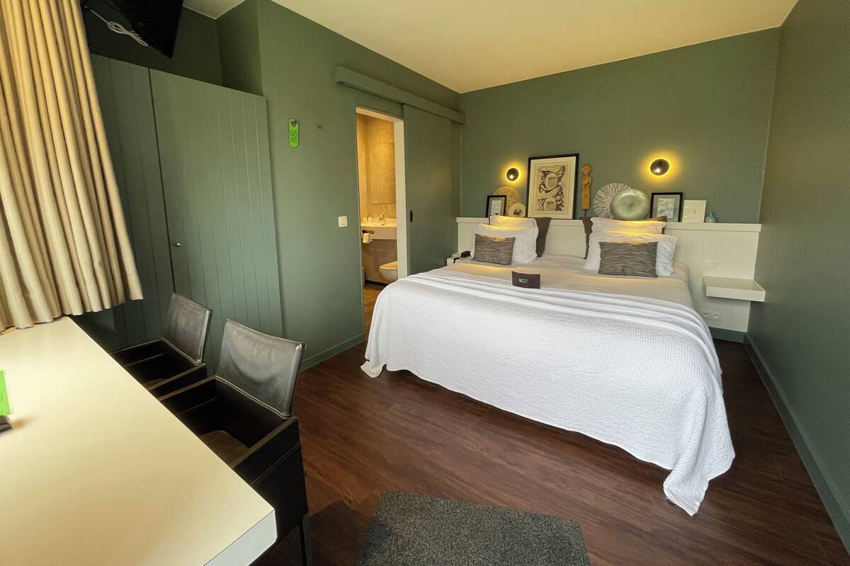 A hotel room with a bed, bedside tables, a desk, and a chair.