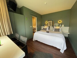 Quarto de hotel com cama, mesas de cabeceira, escrivaninha e uma cadeira.