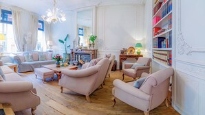 A spacious living room with a sofa, armchairs, a coffee table, and a fireplace. There are bookshelves and a chandelier. - Hotel Montanus (Bruges)