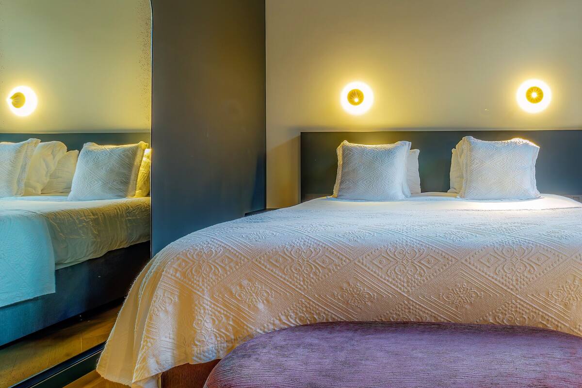 A hotel room with two beds, each with white linens and pillows, and a large mirror on one wall.