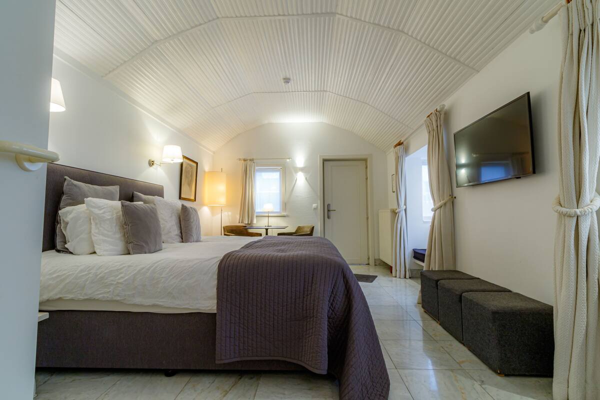A bedroom with a bed, bedside tables, a TV, and a window with curtains.
