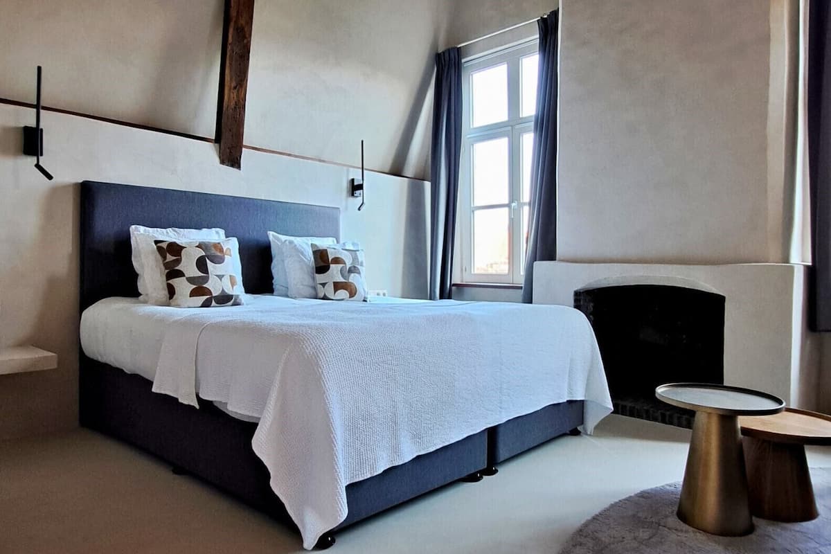 A modern bedroom with a large bed, a fireplace, and a round table.