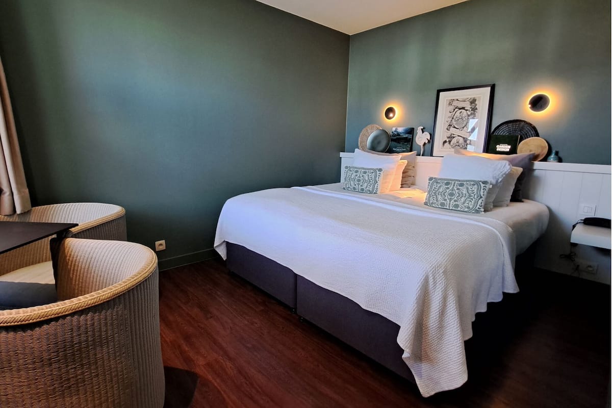 A bedroom with a bed, two bedside tables, a chair, and wall-mounted lights.