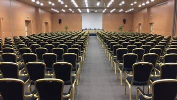 Un salón de conferencias con filas de sillas y un escenario al frente.