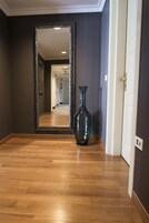 Um corredor com piso de madeira, um espelho grande e um vaso.