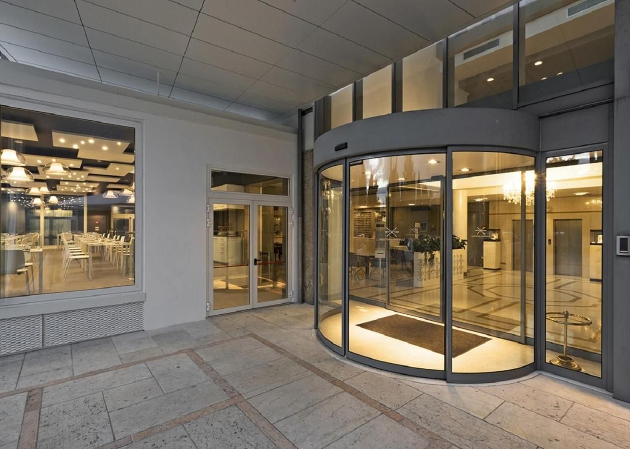 Rebedor modern d'hotel amb una porta giratòria de vidre, zona de seients amb taules i cadires, i una recepció.