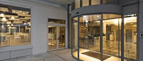 A modern hotel lobby with a glass revolving door, a seating area with tables and chairs, and a reception desk.