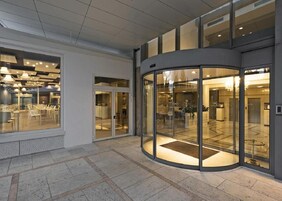 Un vestíbulo de hotel moderno con una puerta giratoria de vidrio, una zona de estar con mesas y sillas, y un mostrador de recepción.
