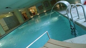 An indoor swimming pool with clear water, metal ladders, and wooden deck area. - Hotel Maggior Consiglio (Treviso)