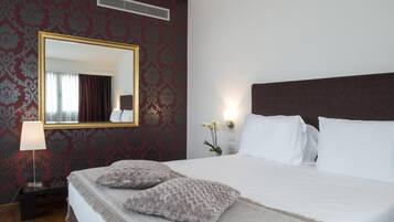 Habitación de hotel con una cama grande, un espejo, una mesita de noche con una lámpara y un papel tapiz decorado.