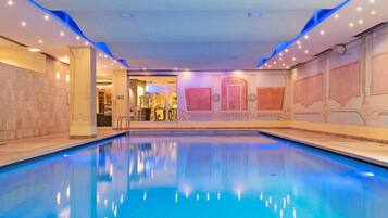 A large indoor swimming pool with clear blue water, surrounded by walls with decorative panels and lighting.