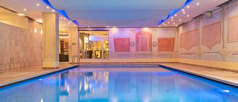 Una amplia piscina interior con agua cristalina y paredes decoradas con paneles e iluminación.