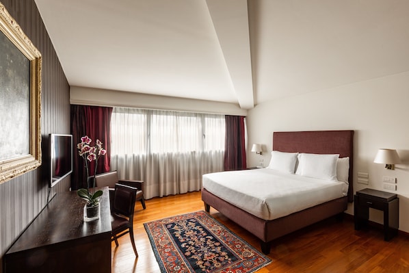 A hotel room with a large bed, a desk with a chair, a TV, and a window with curtains.