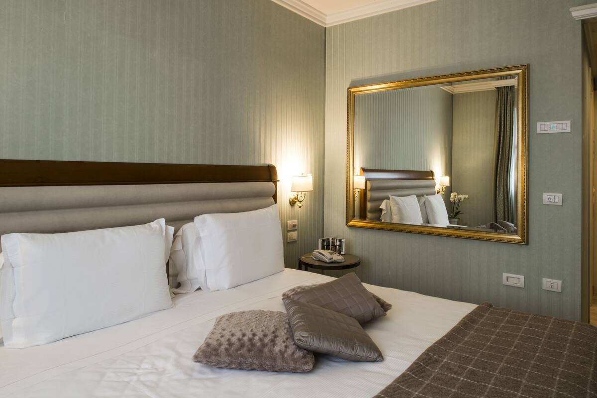 A hotel room with a large bed, a nightstand, a mirror, and a lamp.