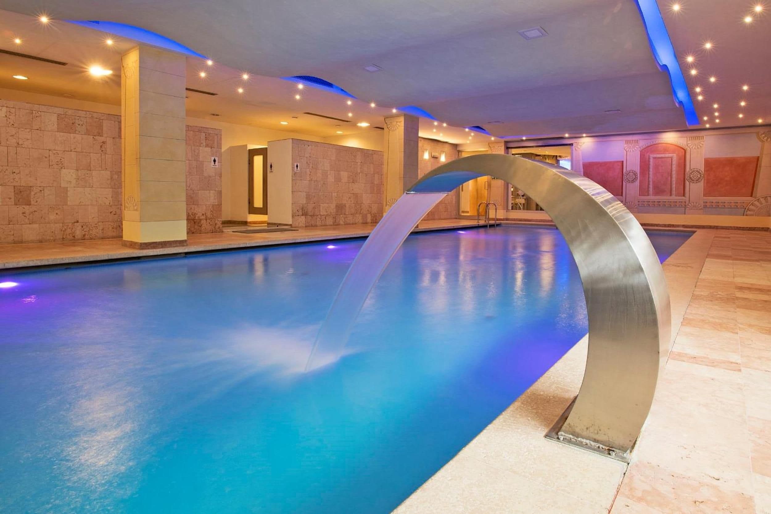 Una piscina interior con diseño moderno, que incluye una estructura de vidrio curvada y una pared de piedra.