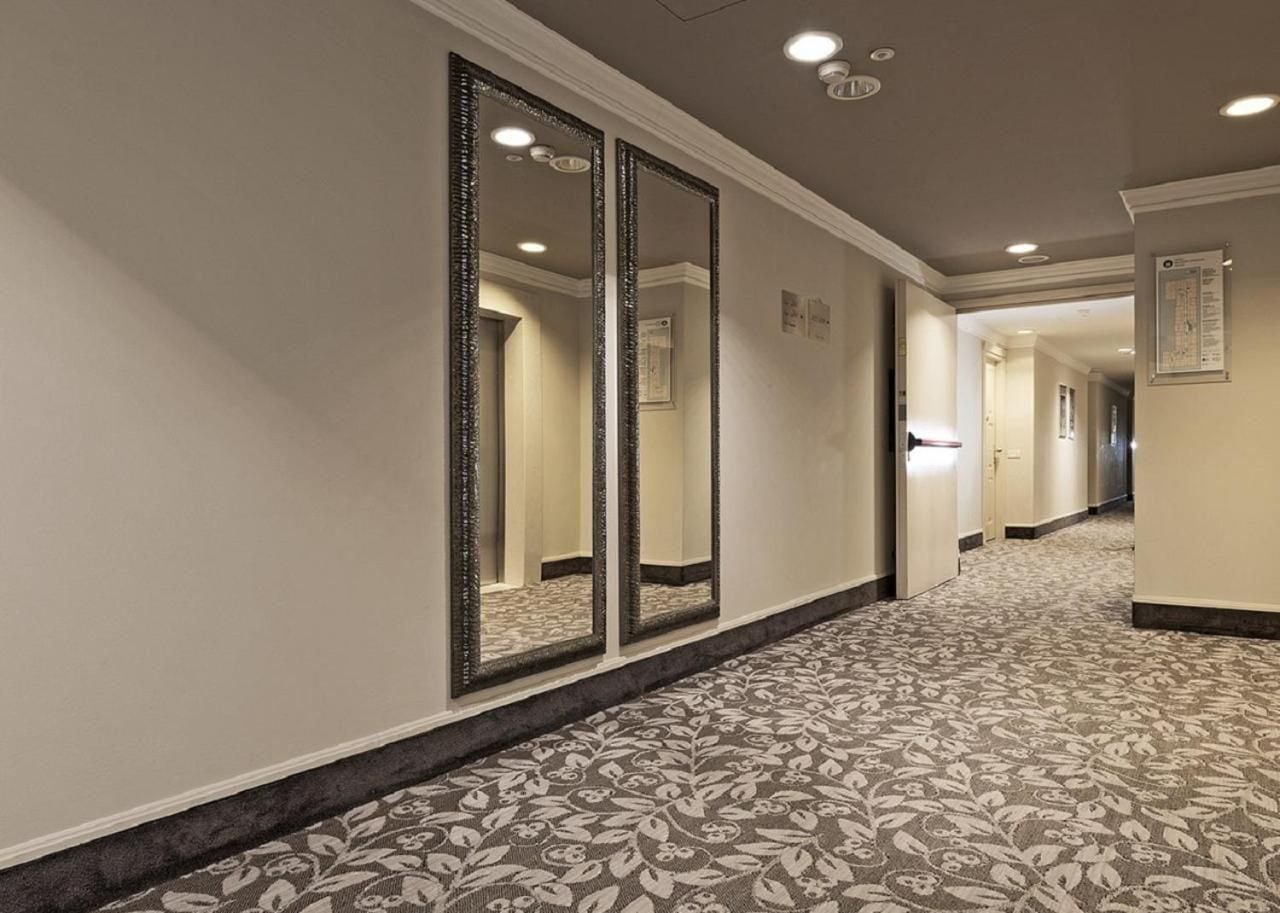 A hallway with a patterned carpet, large mirrors, and recessed lighting.