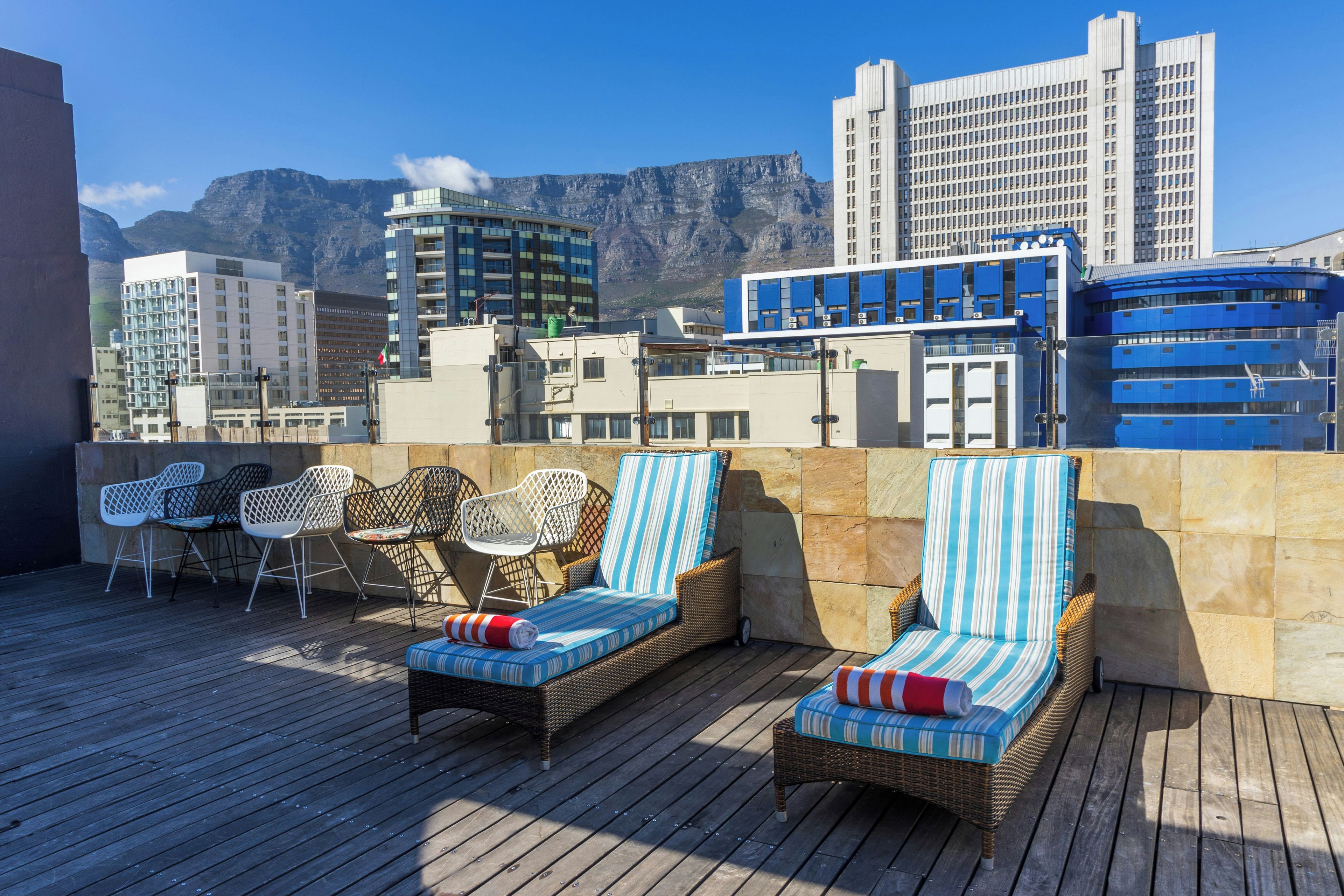 A rooftop terrace with wicker lounge chairs and a view of city buildings and mountains.