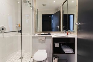 A modern bathroom with a glass shower enclosure, a white toilet, a sink with a mirror above, and a dark-toned vanity.
