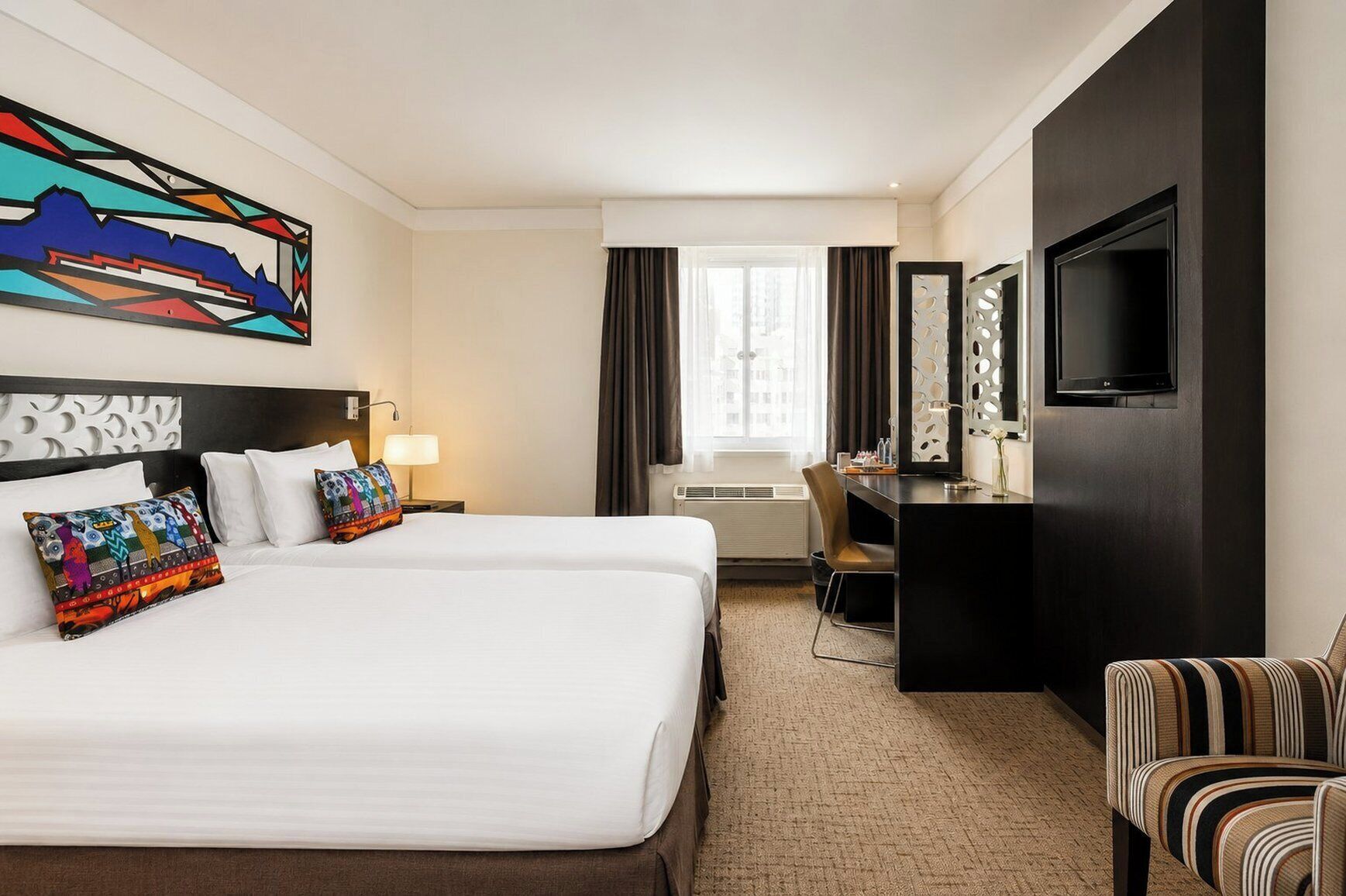 Een hotelkamer met twee bedden, een bureau, een televisie en een groot raam.