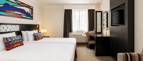 A hotel room with two beds, a desk, a TV, and a large window.
