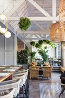 A spacious indoor area with high ceilings, hanging plants, wicker furniture, and a patterned floor.
