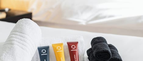 Habitación de hotel con una cama bien tendida, un juego de artículos de tocador que incluye gel de ducha, loción corporal y una toalla, además de un cuadro en la pared.
